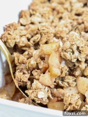 Apple and pear crumble in a white baking dish with a gold spoon.