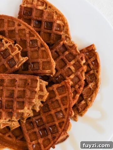 Quarters of round pumpkin waffles overlapping and topped with a drizzle of maple syrup on a white plate.