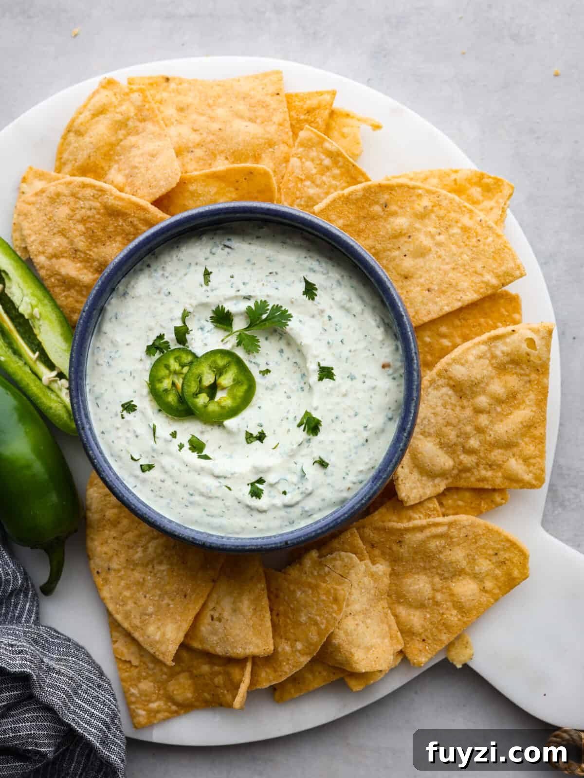 Serve with chips or vegetables. The top view of a platter of tortilla chips with a bowl of jalapeño dip with a sliced jalapeño garnishing the dip.