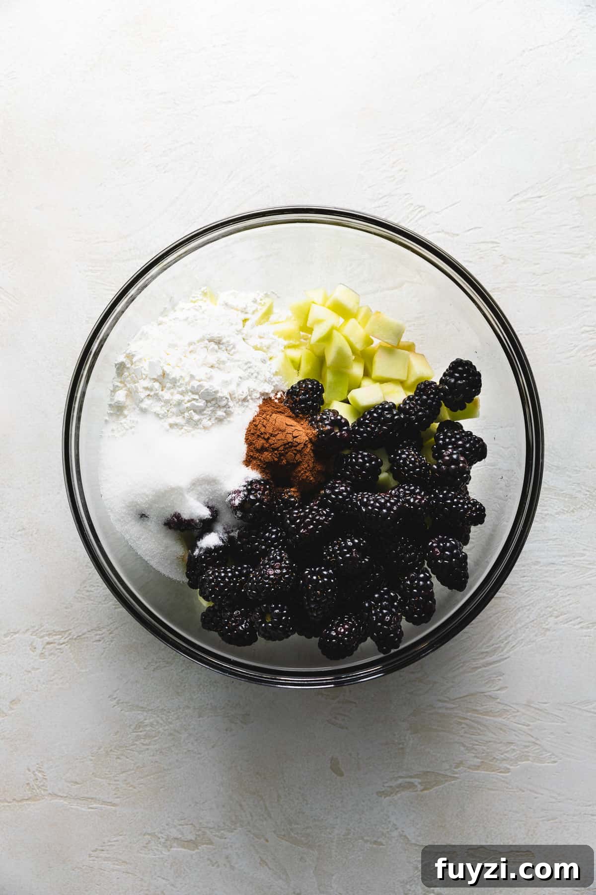 Flour, sugar, spices, apples, and blackberries in a bowl.