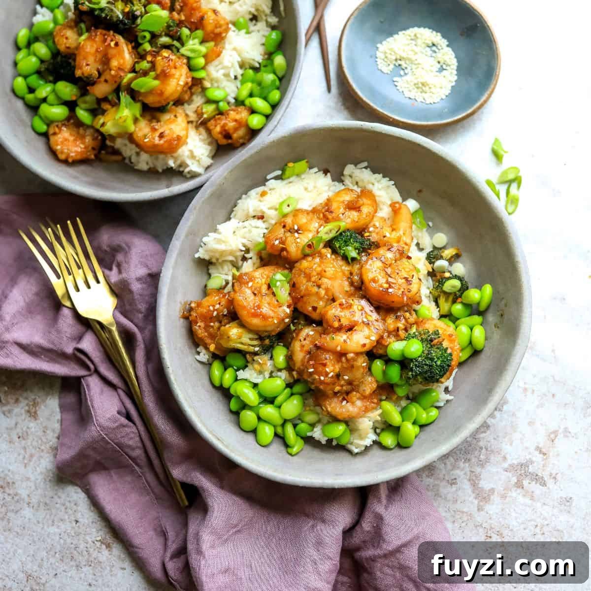 Grey ceramic bowls with rice and Mongolian shrimp with gold forks.