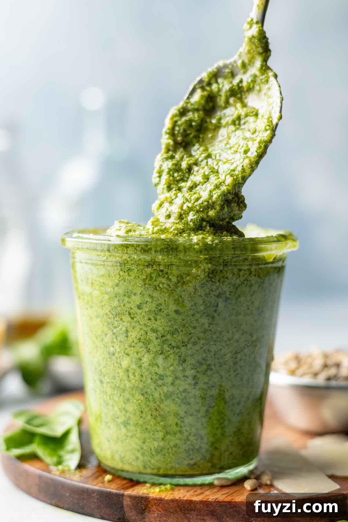 Pesto sauce without pine nuts drips from spoon into small jar.