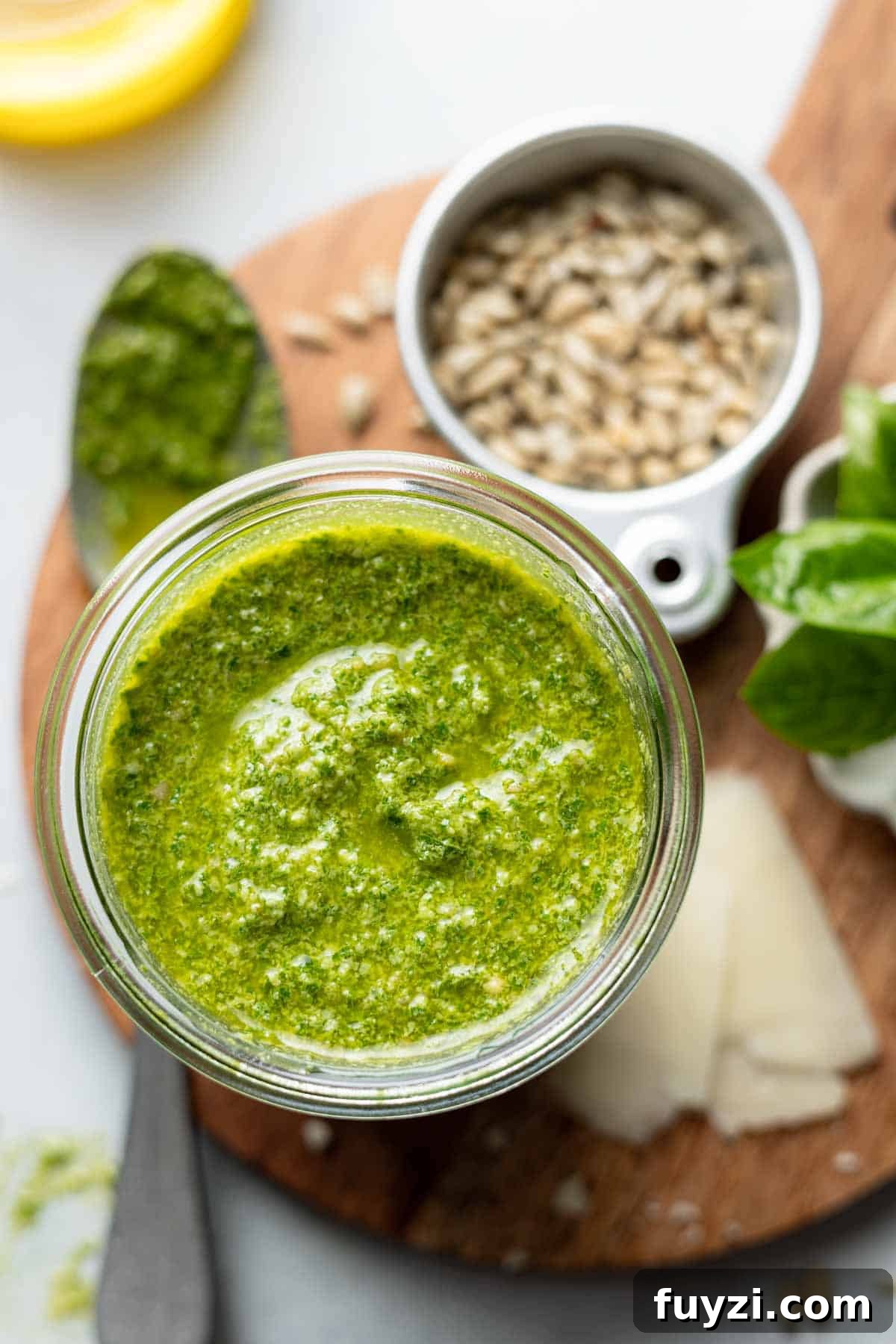 Jar filled with basil pesto without pine nuts, next to small bowl of sunflower seeds.