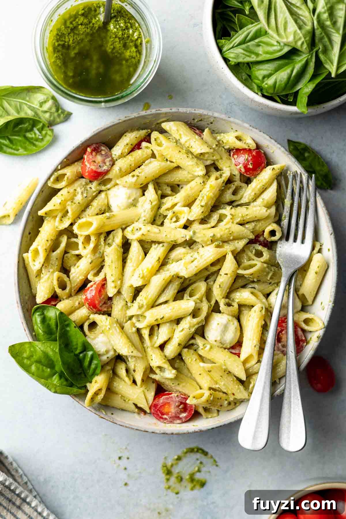 Pasta in large bowl tossed with creamy pesto sauce, tomatoes, and fresh mozzarella.