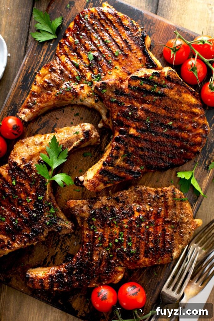 Four golden brown grilled pork chops on a wooden board