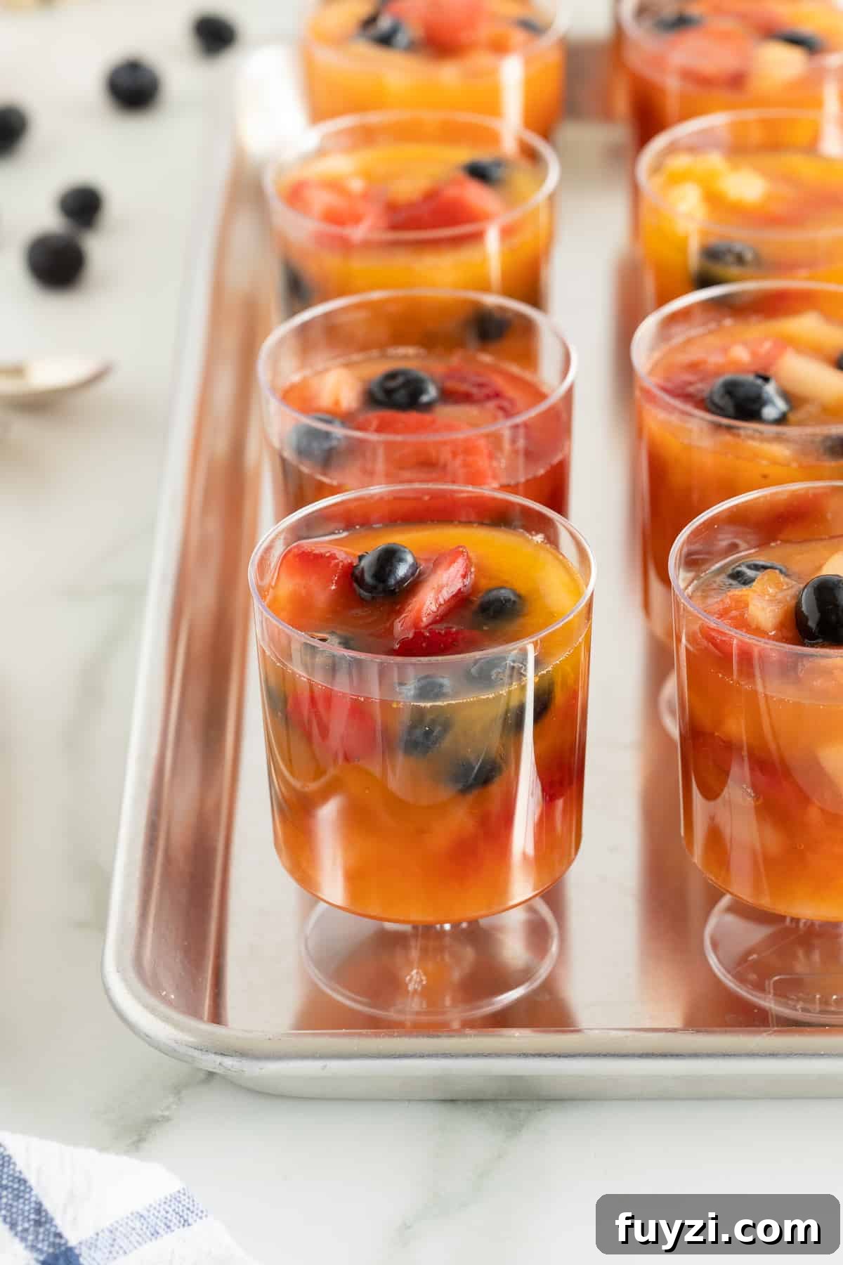 A close up of plastic cups filled with frozen fruit on a baking sheet.