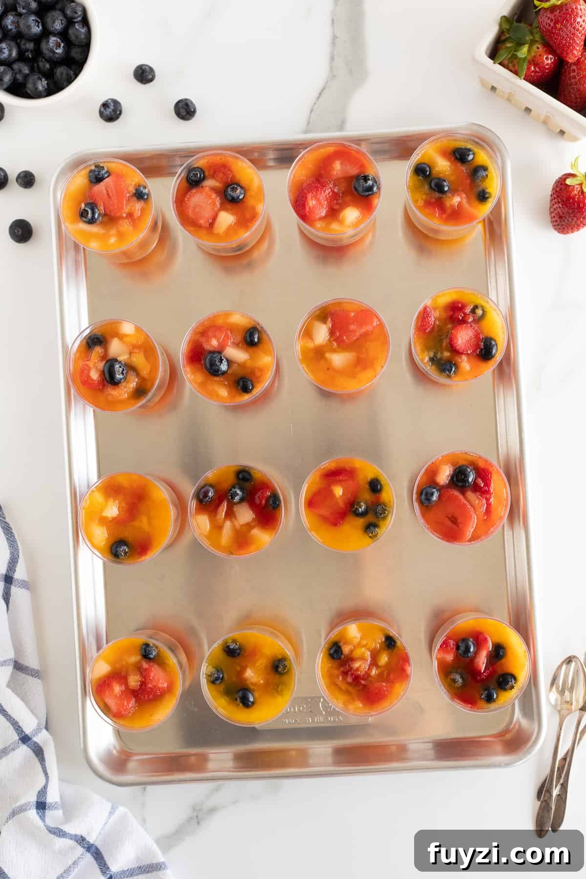 A top down shot of plastic cups filled with frozen fruit on a baking sheet.