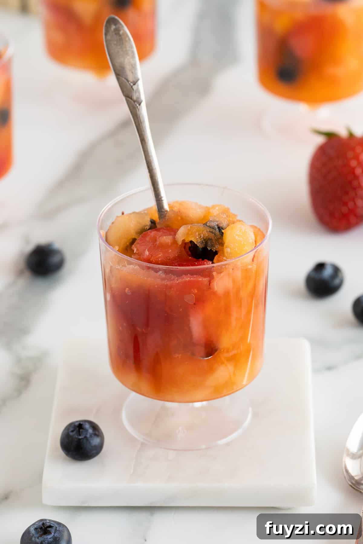 A spoon stuck into a plastic cup of slushy frozen fruit.