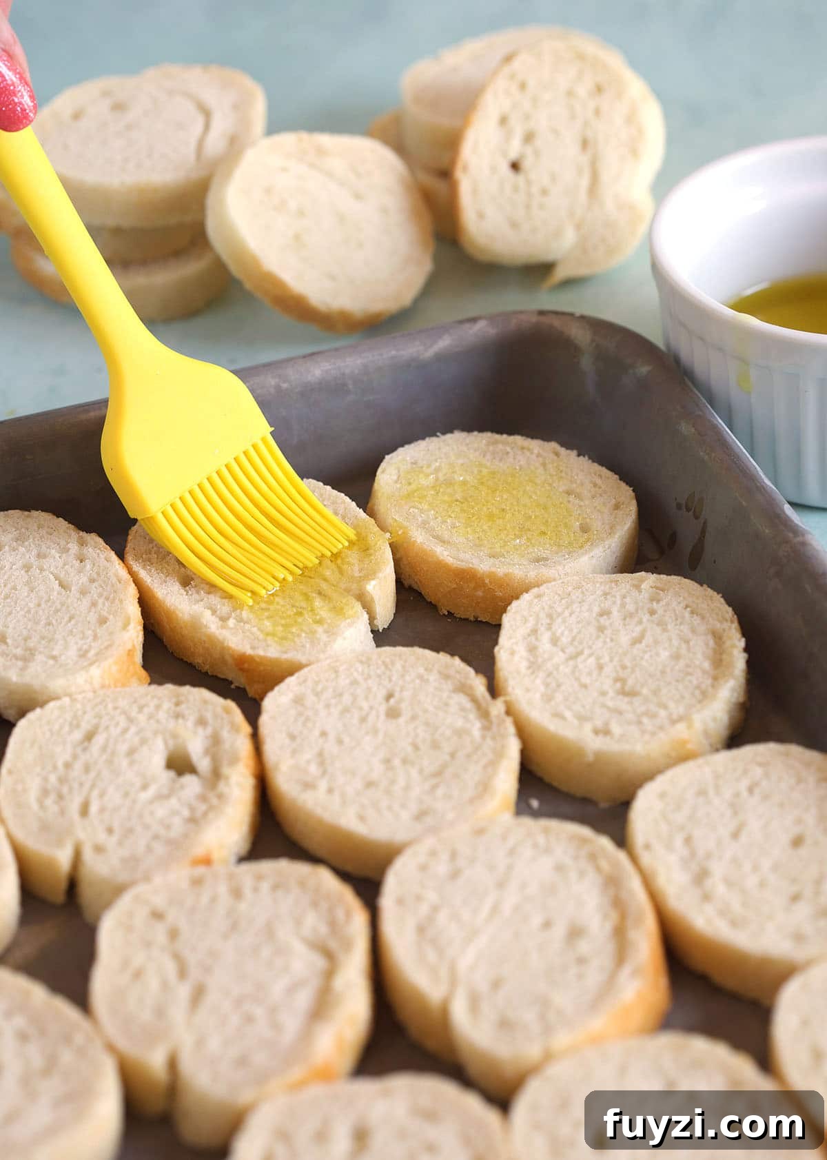 How to Make Crostini: Crispy Homemade Bread and Topping Ideas 4 A yellow rubber brush is brushing butter onto slice of crostini.