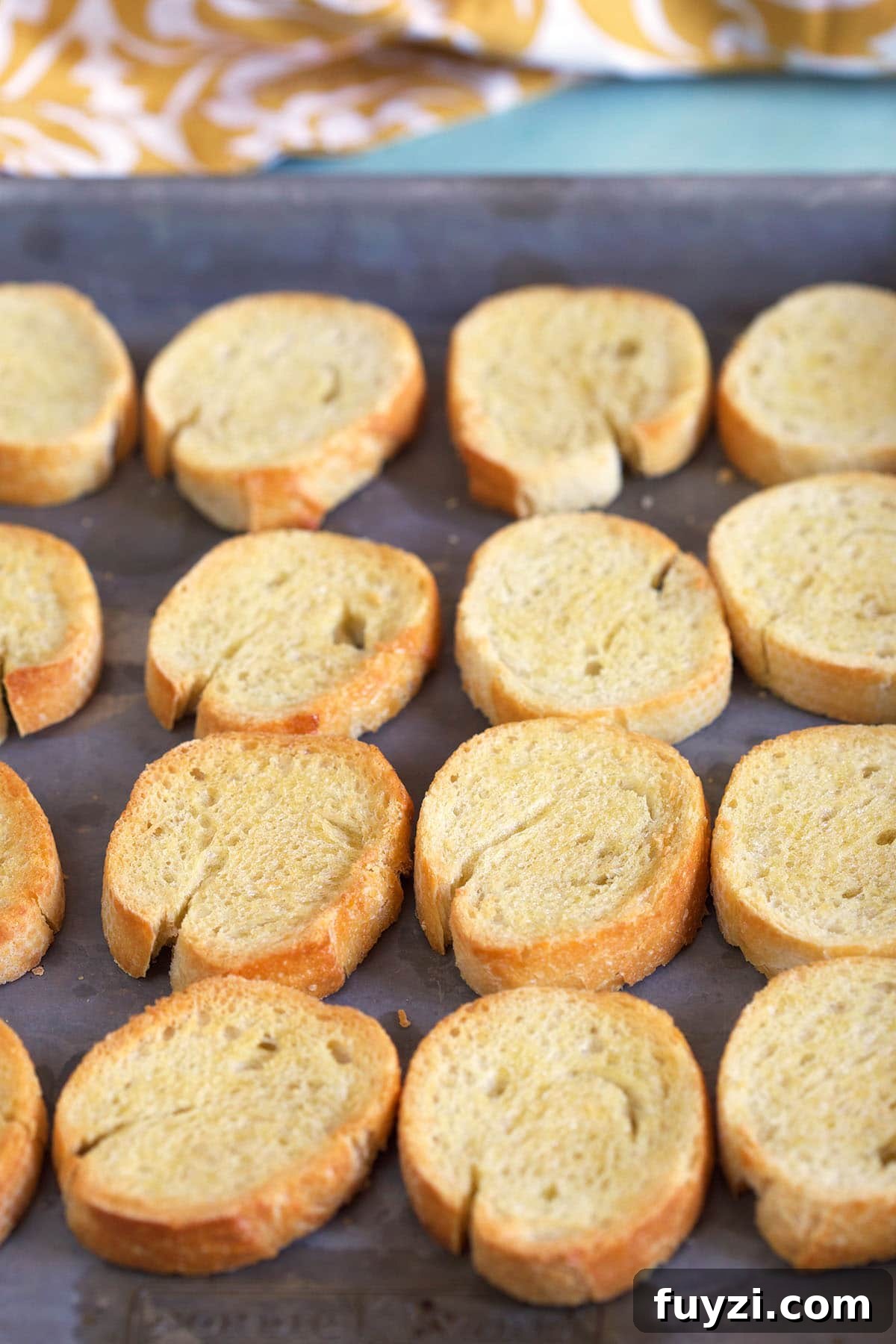 How to Make Crostini: Crispy Homemade Bread and Topping Ideas 5 Slices of toasted crostini are on a baking sheet.