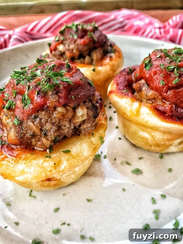 Three meatball cups on a plate. They are meatballs in dough cups with a little tomato sauce on top.