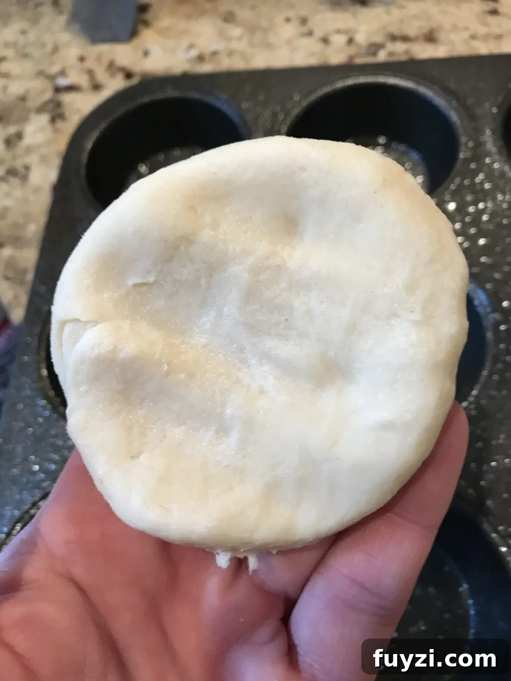 A circle of dough held above a muffin tray.
