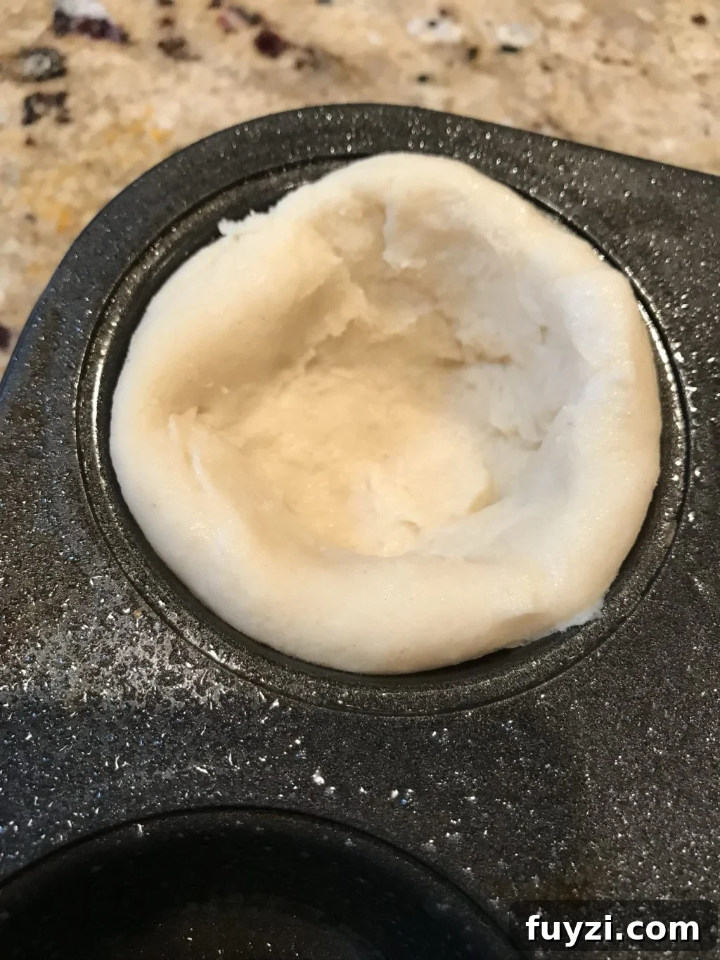 Dough pressed into a muffin tin.