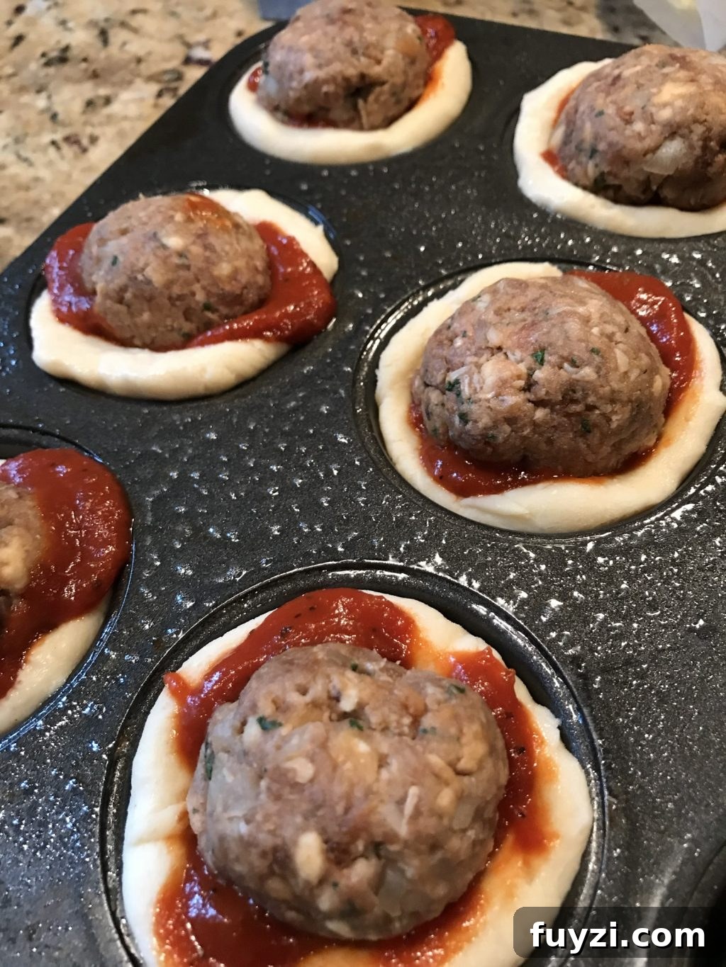 Raw meatballs in sauce in the raw dough in the muffin tin.