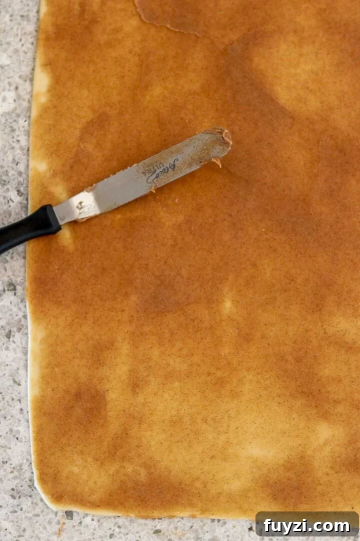 Swedish Cinnamon Bun (Kanelbullar) dough spread with cinnamon sugar filling with an offset spatula.