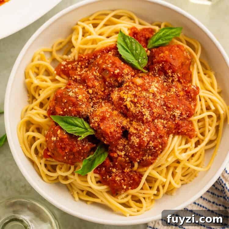 Gluten free meatballs in tomato sauce spooned over a bowl of spaghetti garnished with fresh basil leaves.
