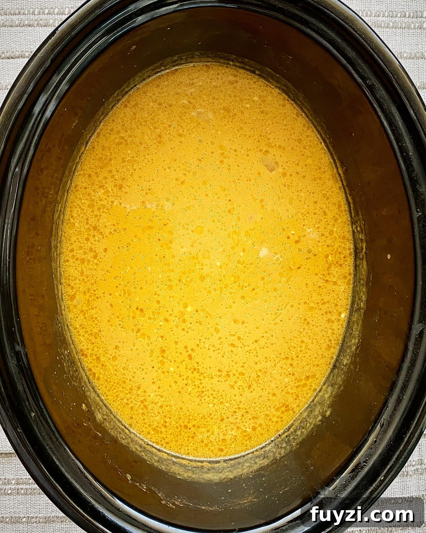 Creamy Slow Cooker Pumpkin Bisque 5 overhead shot of cooked crockpot pumpkin bisque in a black slow cooker