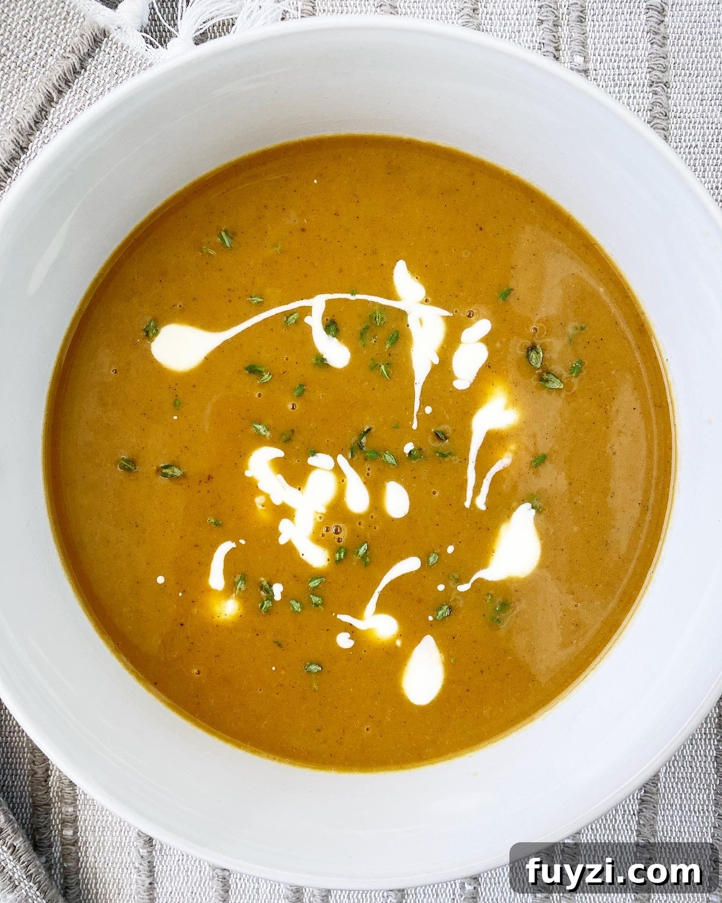 Creamy Slow Cooker Pumpkin Bisque 8 overhead shot of pumpkin bisque in a white bowl garnished with fresh thyme and a drizzle of coconut milk