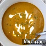 overhead shot of pumpkin bisque in a white bowl garnished with fresh thyme and a drizzle of coconut milk