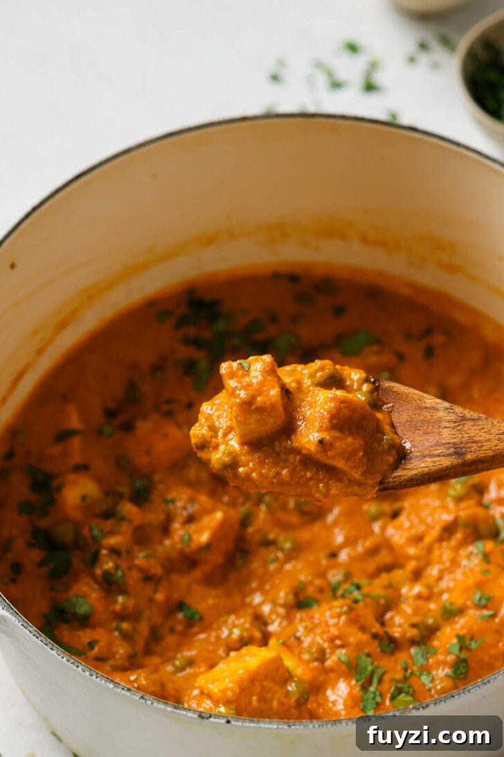 Authentic Restaurant-Style Matar Paneer Recipe 3 Holding a spoonful of saucy Paneer cubes over a dutch oven.