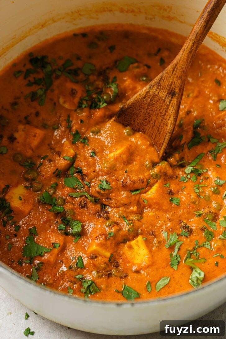 Authentic Restaurant-Style Matar Paneer Recipe 5 Close up of Matar Paneer in a dutch oven with a wooden spoon and garnished with cilantro.