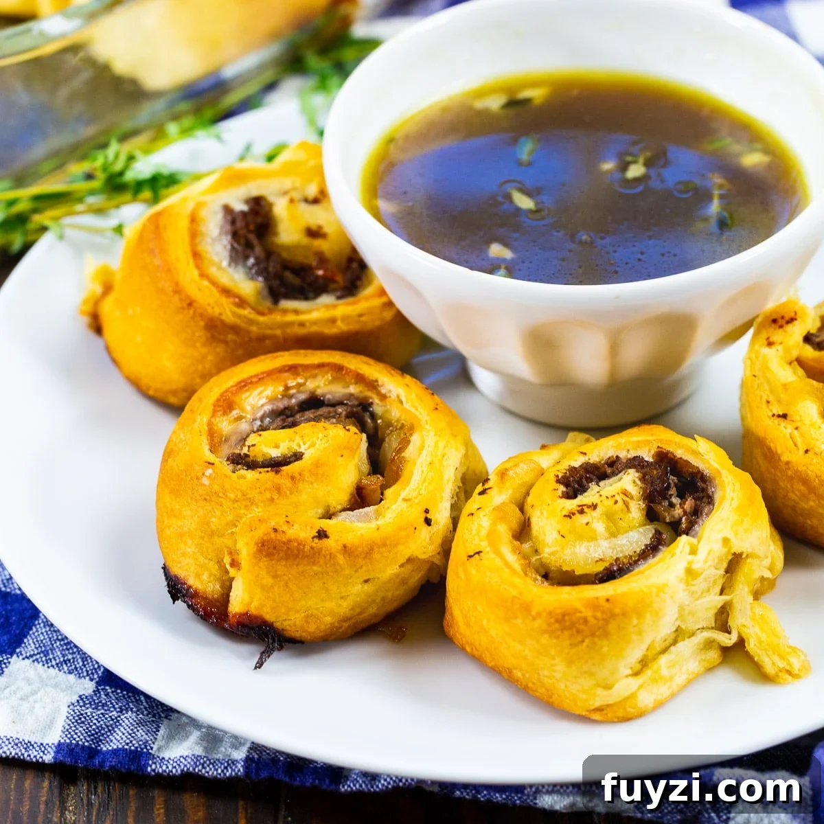 French Dip Pinwheels Recipe: Party Appetizer with Au Jus 2 French Dip Pinwheels on a plate with a bowl of Au Jus.