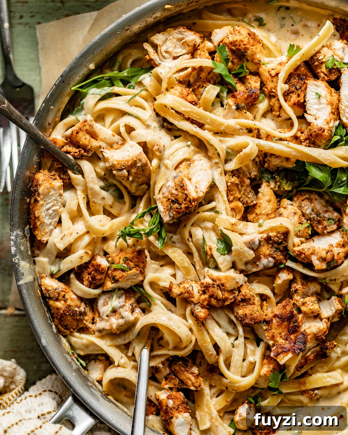 up close photo of chicken alfredo in a skillet with forks and garlic bread.