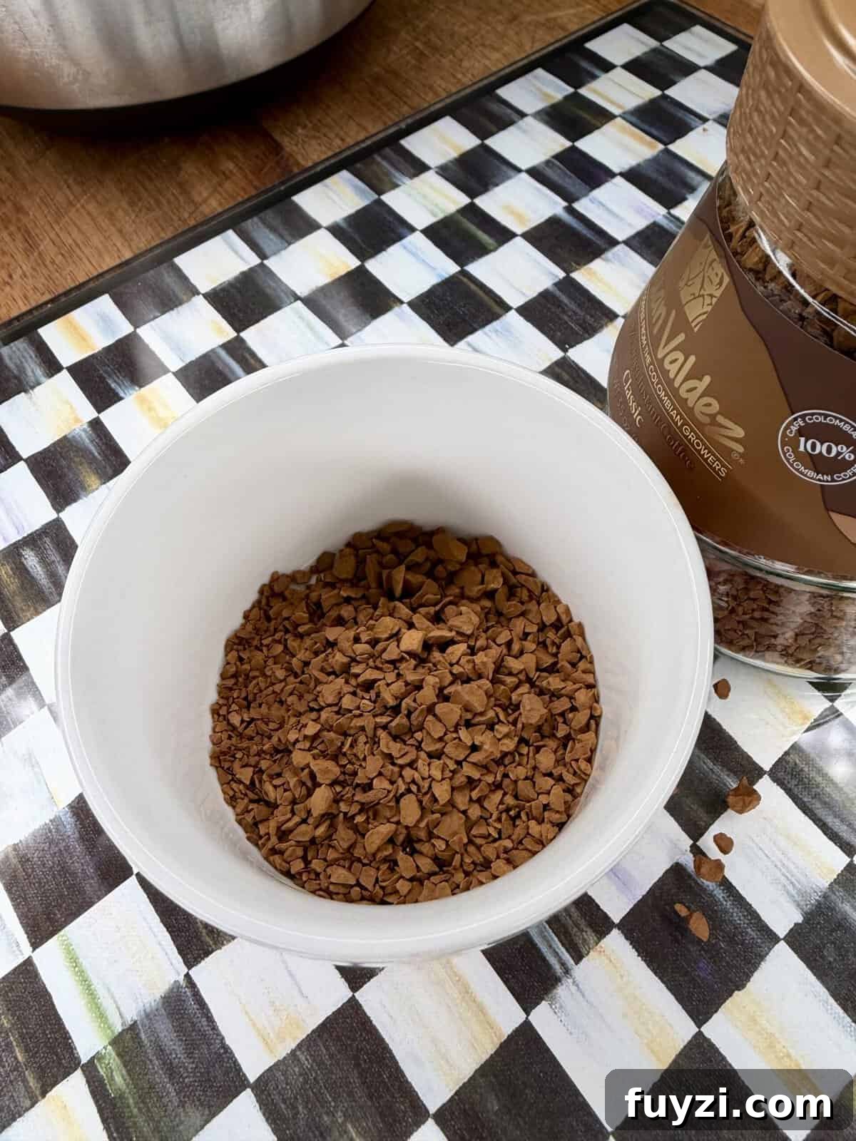 No-Bake Vintage Coffee Ice Cream Pie Recipe 5 A white cup filled with instant coffee granules sits on a checkered surface next to an open jar of coffee.