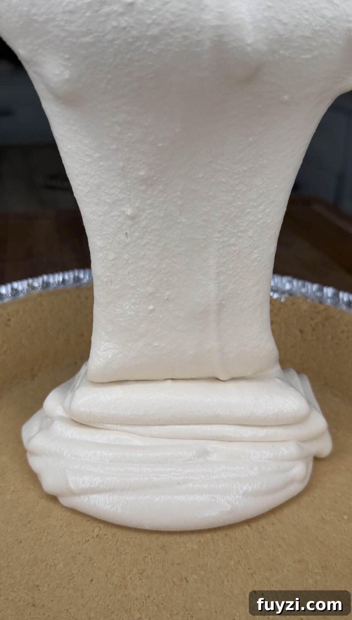 No-Bake Vintage Coffee Ice Cream Pie Recipe 6 Thick, creamy white filling is being poured into a pie crust, forming smooth, layered folds as it settles in an aluminum pie tin.