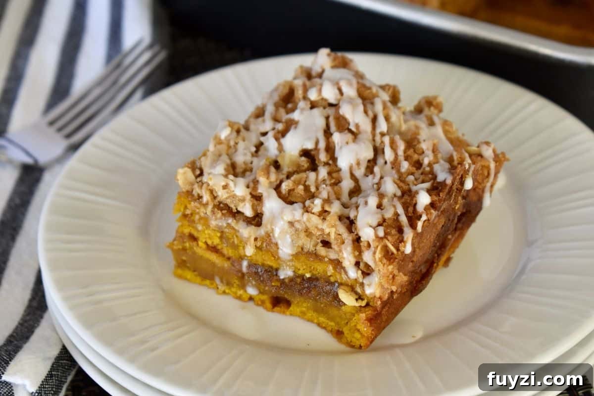 Pumpkin Streusel Coffee Cake Recipe with Cinnamon Crumble 7 Slice of pumpkin streusel coffee cake with icing drizzle over top on a white plate.