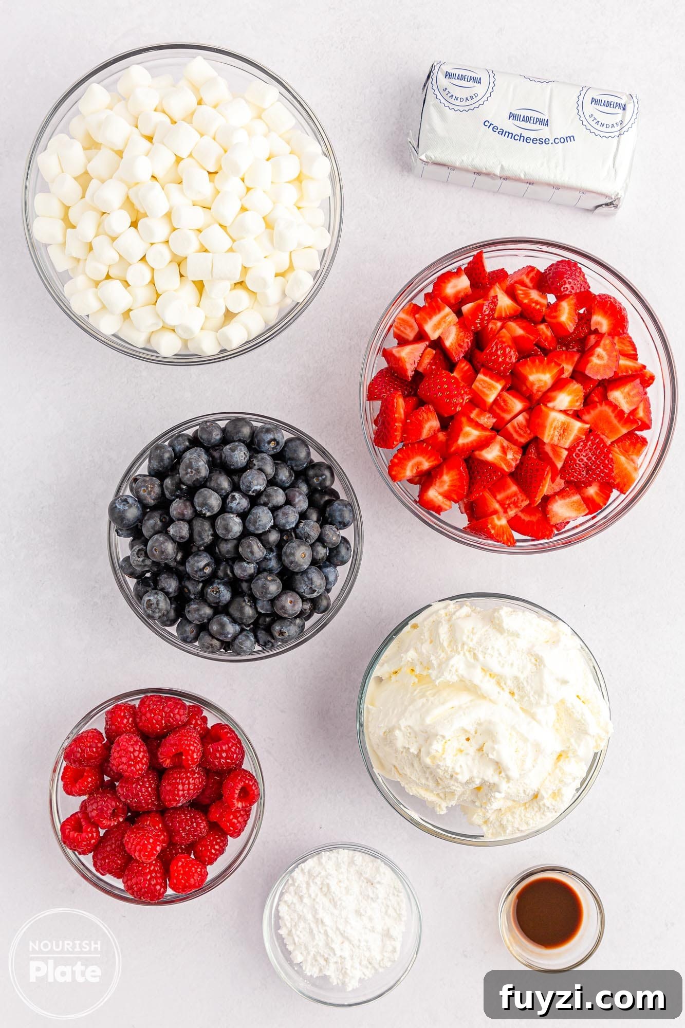 Overhead shot of cheesecake salad ingredients including whipped topping, cream cheese, fresh berries, mini marshmallows, and vanilla.