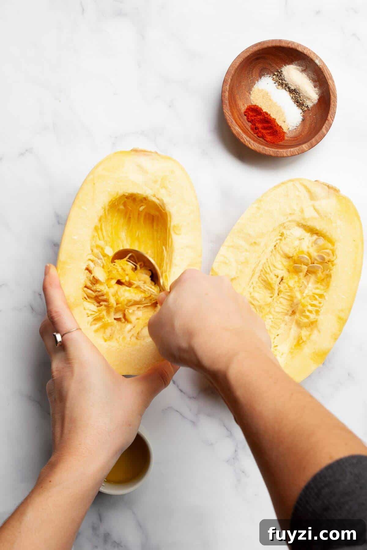 Scooping seeds out of raw spaghetti squash half with a spoon.