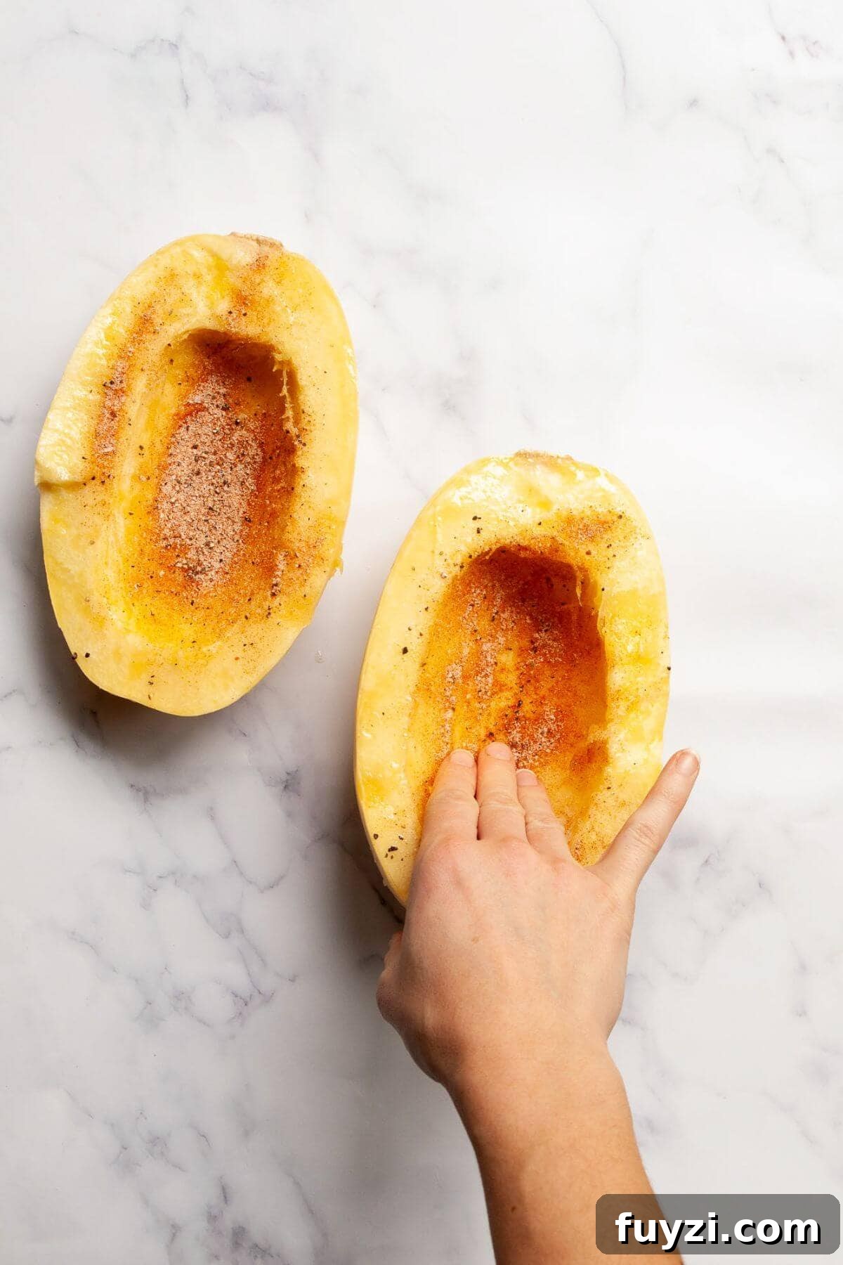 Seasoning spaghetti squash halves with olive oil, salt, pepper, paprika, onion powder, and garlic powder before cooking in the air fryer.
