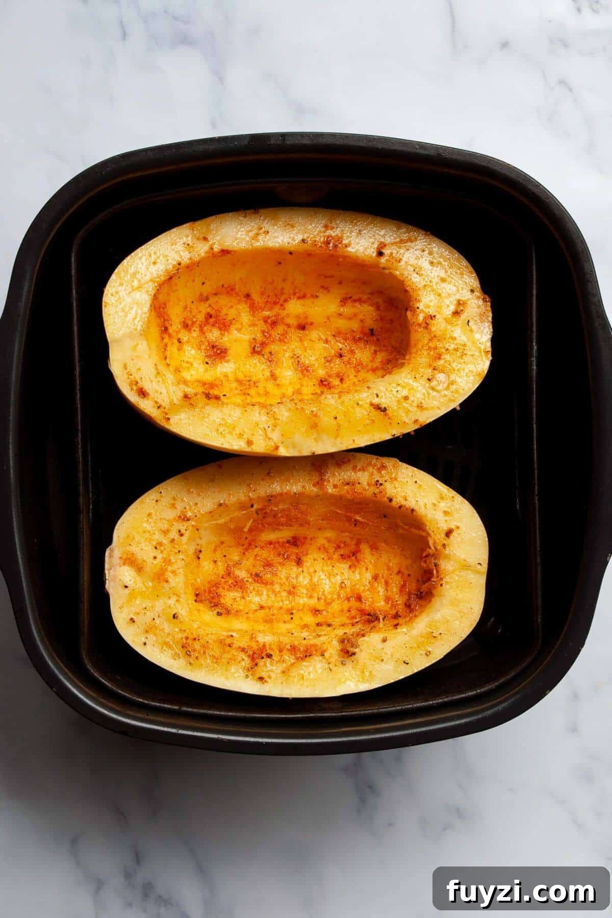 Seasoned spaghetti squash halves ready to cook in the air fryer basket.