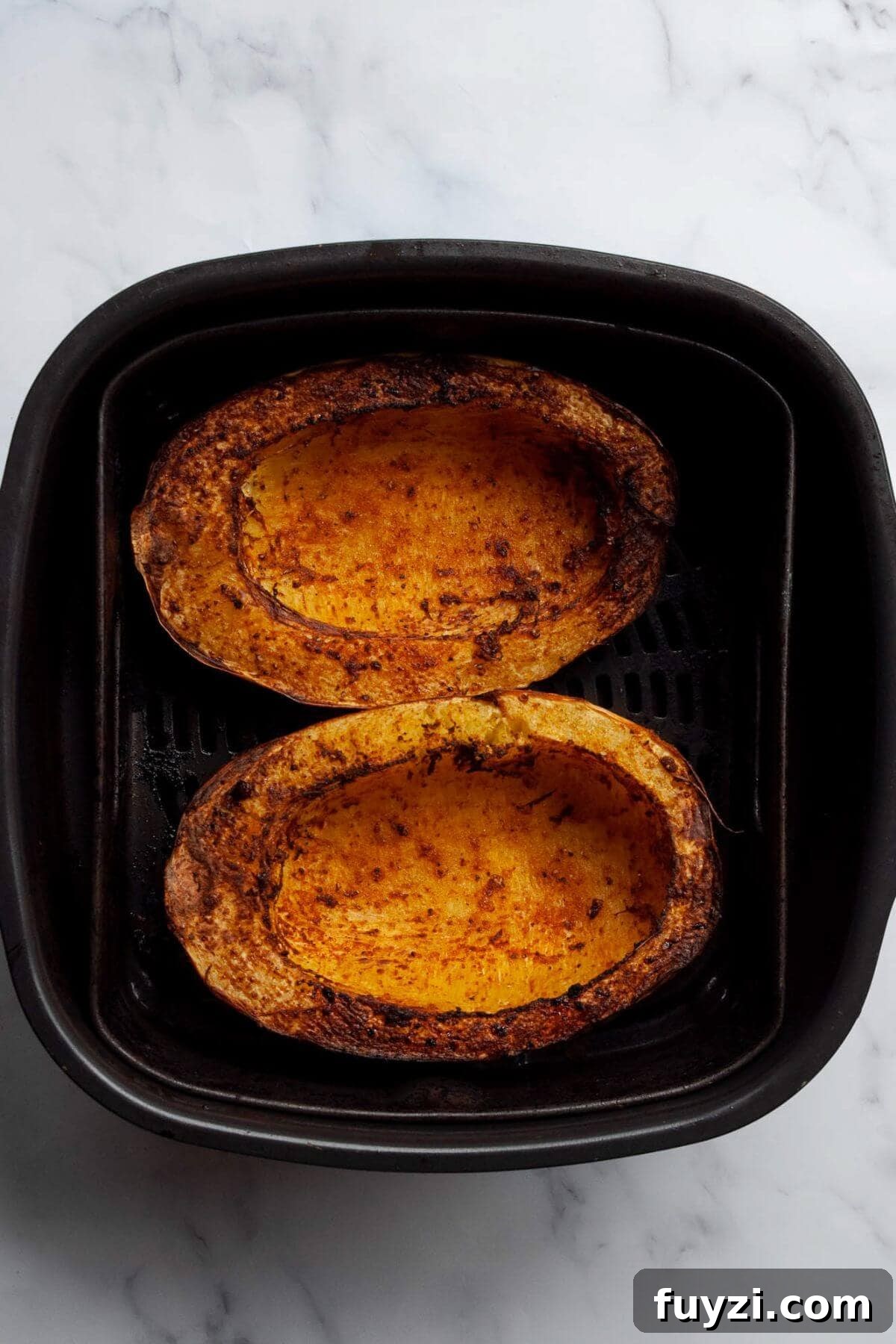 Two fork-tender, crispy cooked spaghetti squash halves sitting in an air fryer basket.