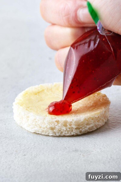 Mini Jam Sandwiches for Afternoon Tea 7 Strawberry jam being piped on top of white bread and butter.