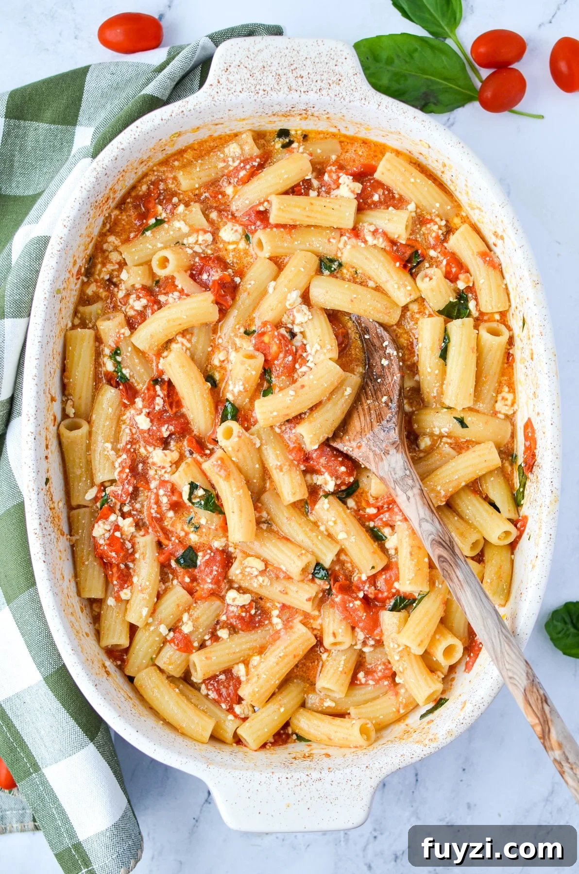 A baking dish with a tomato and pasta dish garnished with basil.