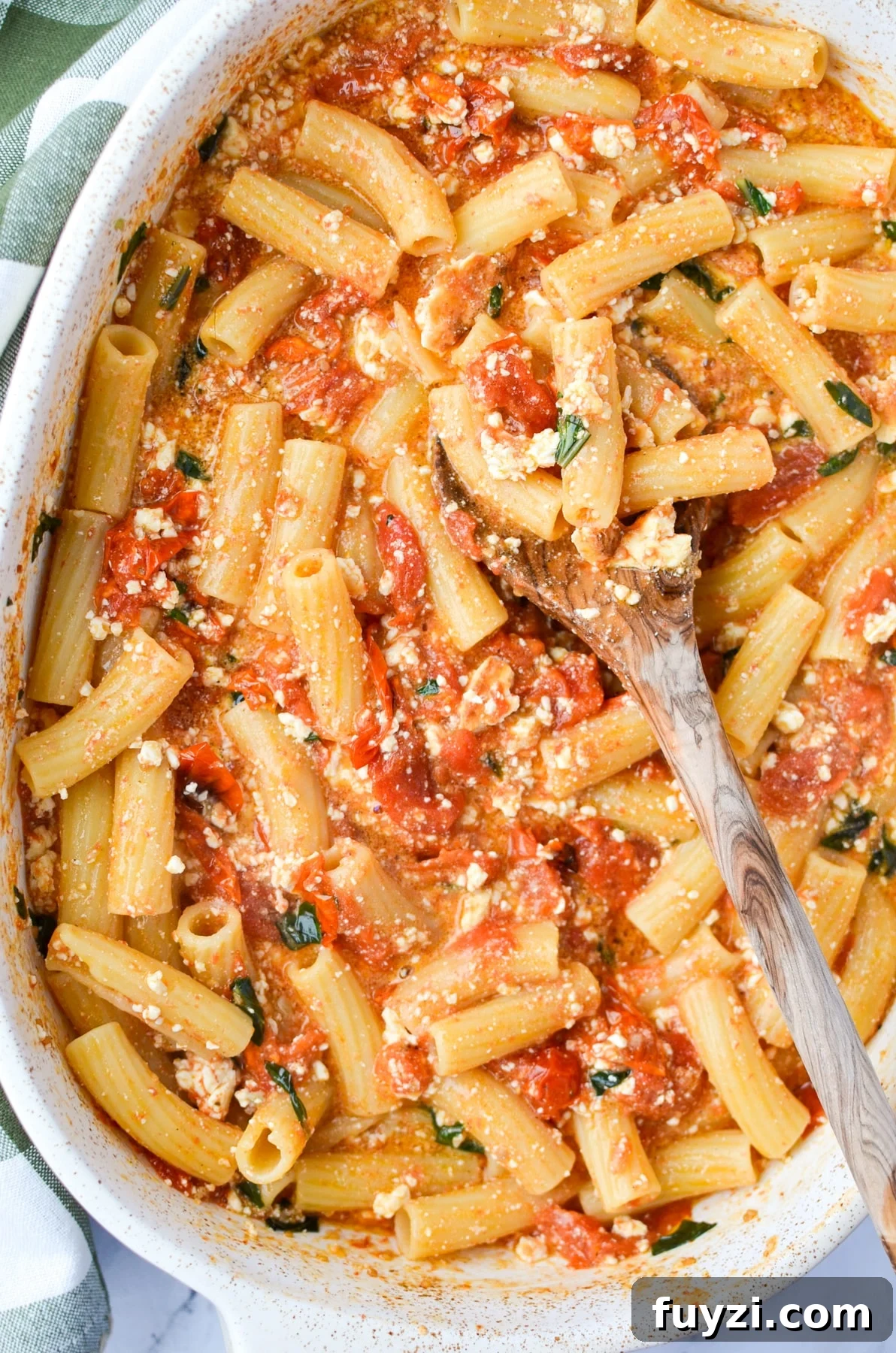 A baking dish with pasta, tomatoes, feta, and basil.