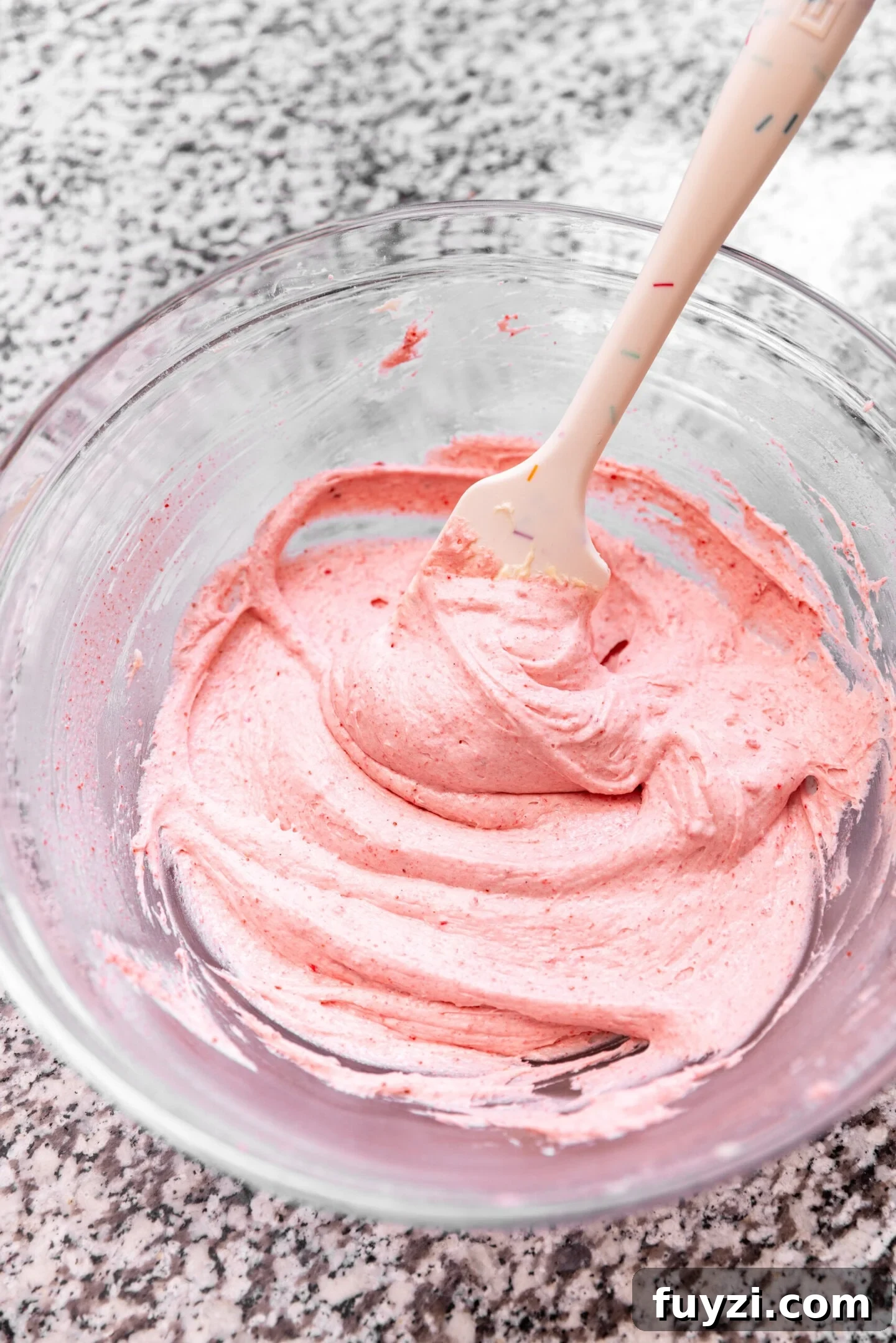 A bowl of silky smooth strawberry cream cheese frosting with a spatula in it.