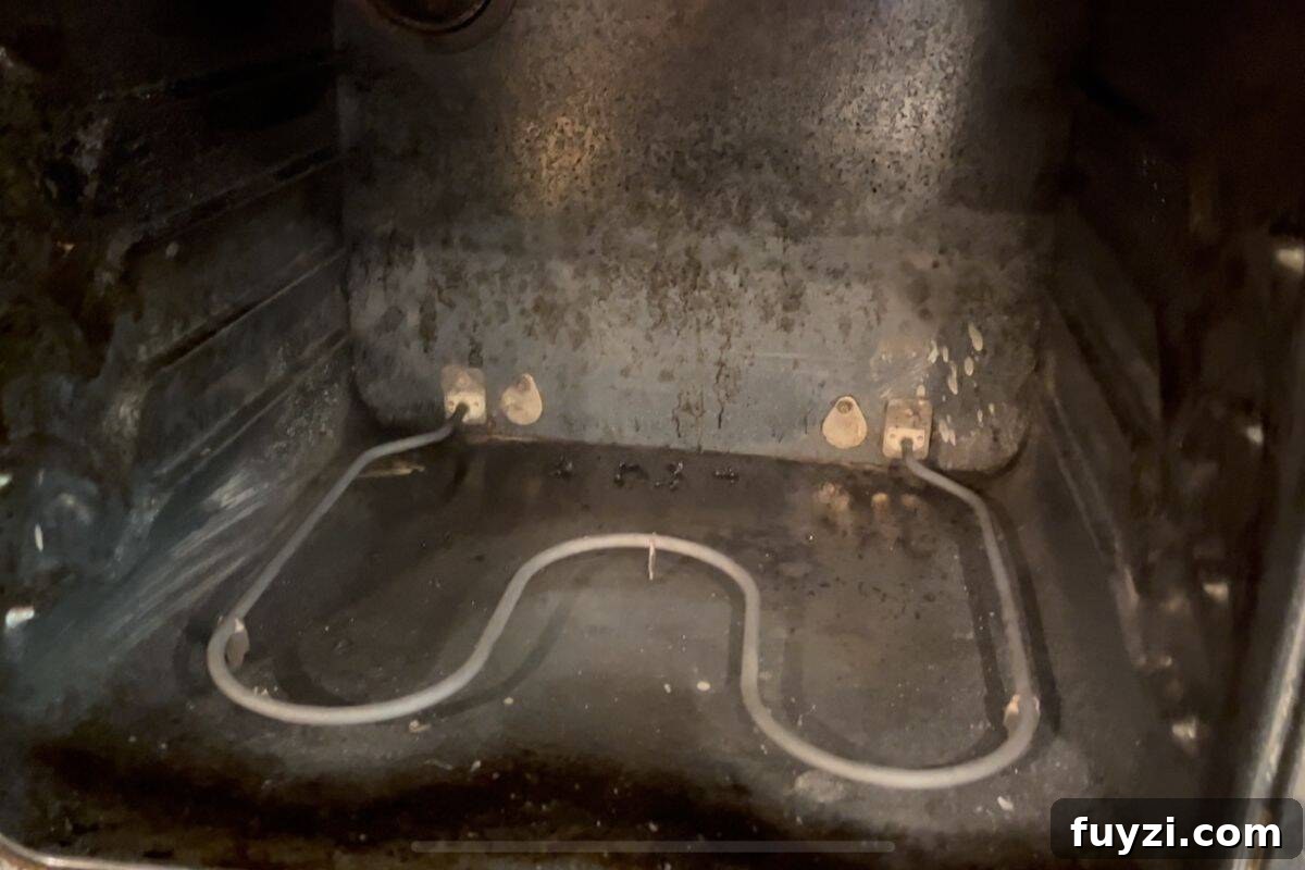 View of the inside of an oven, showing the metal heating element at the bottom and visible grime and stains.