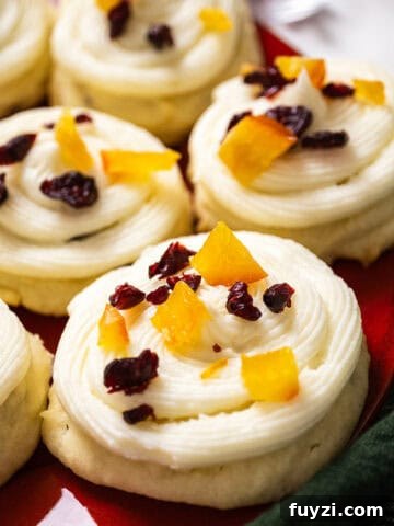 Cranberry and orange shortbread cookies topped with frosting and garnished with dried cranberries and candied oranges.