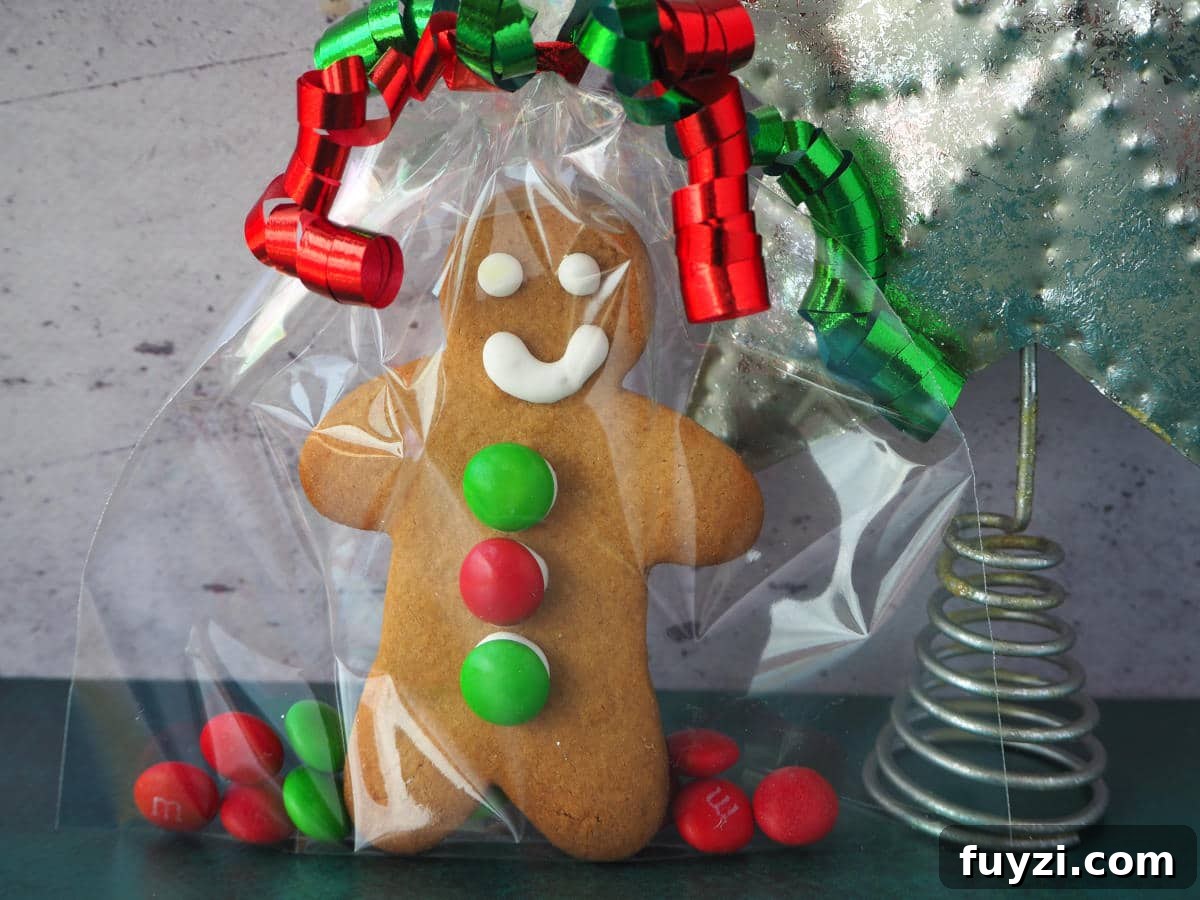 gingerbread man made up as a gift in a clear cellophane bag with red and green M&Ms and green and red curling ribbon around the top, with a silver tree top start to the right.