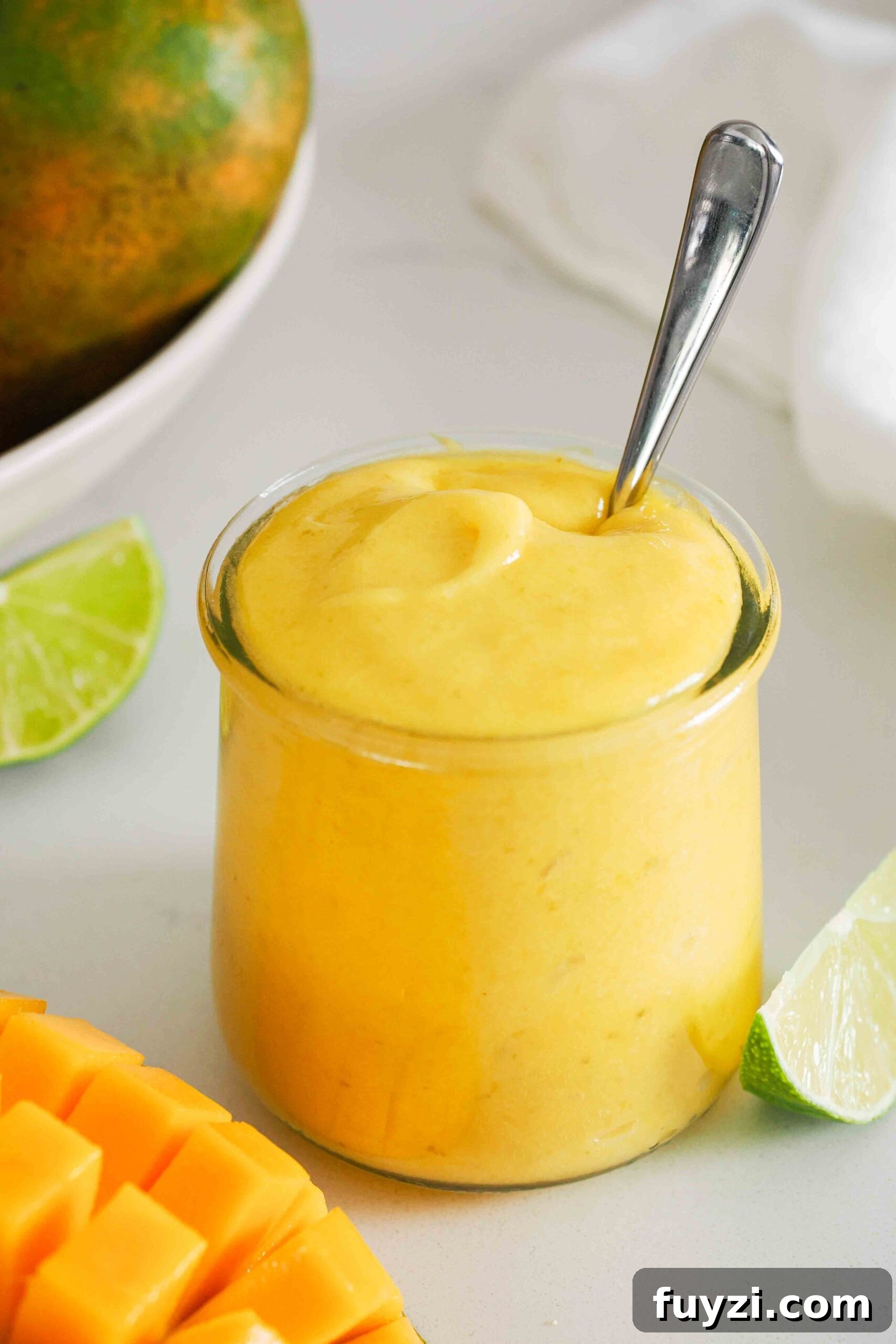A spoon rests in a small jar of small batch mango curd.