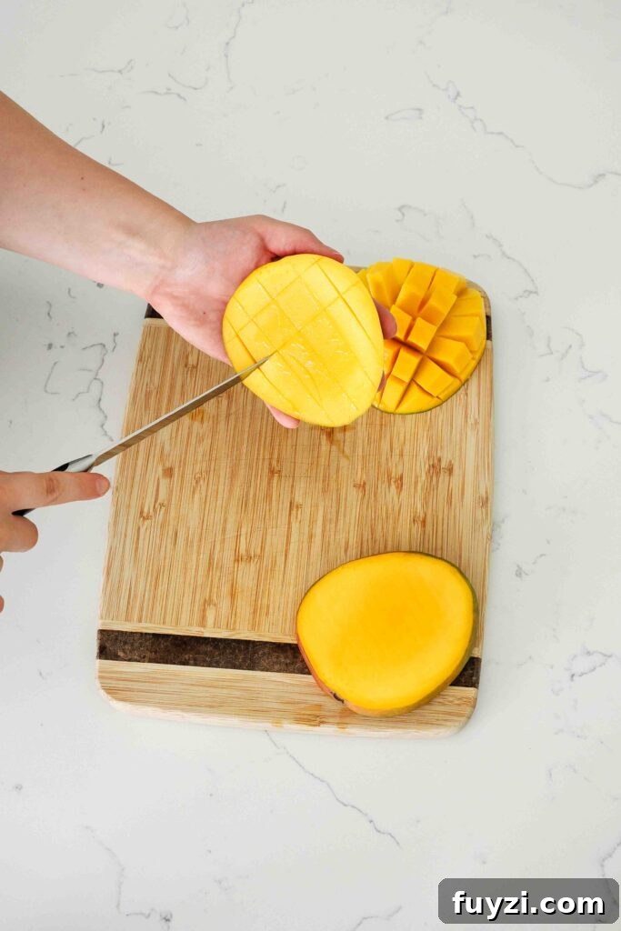 A knife cuts squares into a slice of mango.
