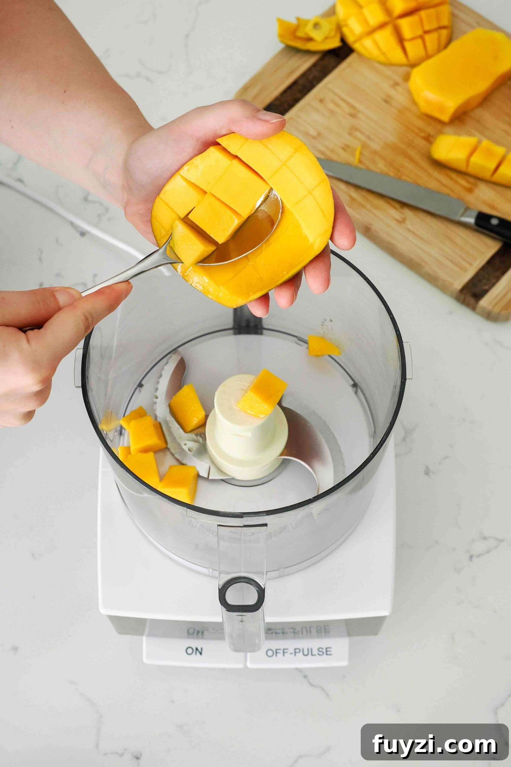A spoon scoops squares of fruit out of a sliced mango.