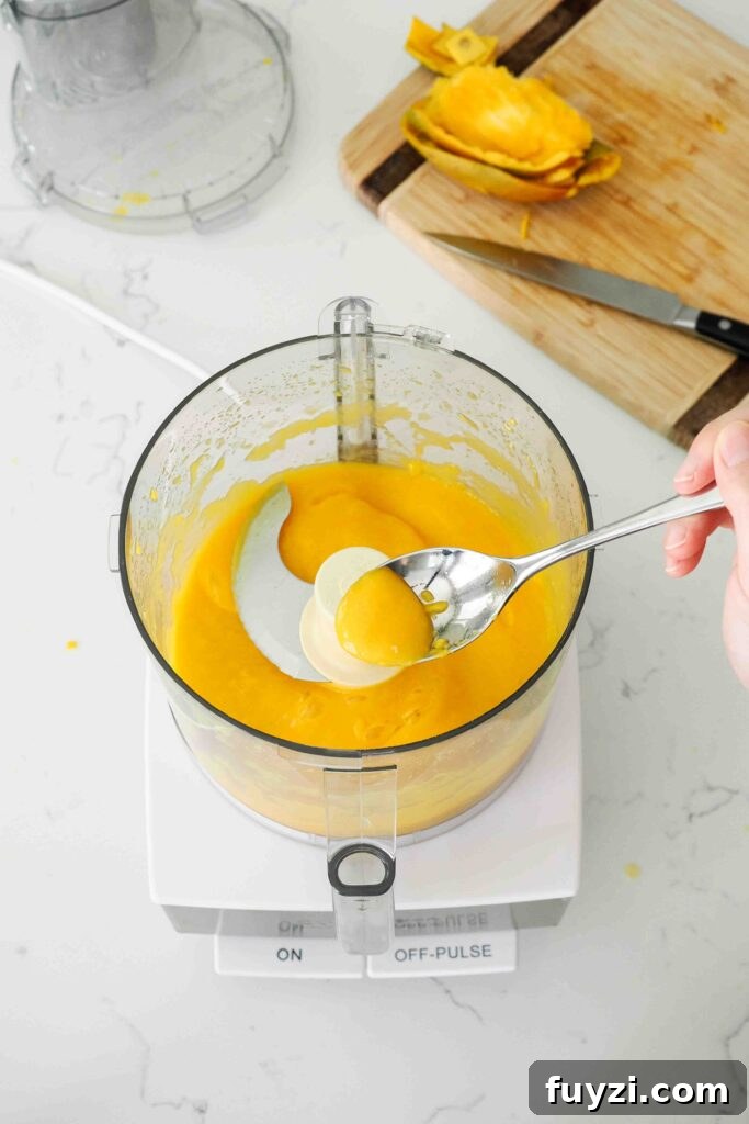 A spoon holds up freshly pureed mango from a food processor bowl.