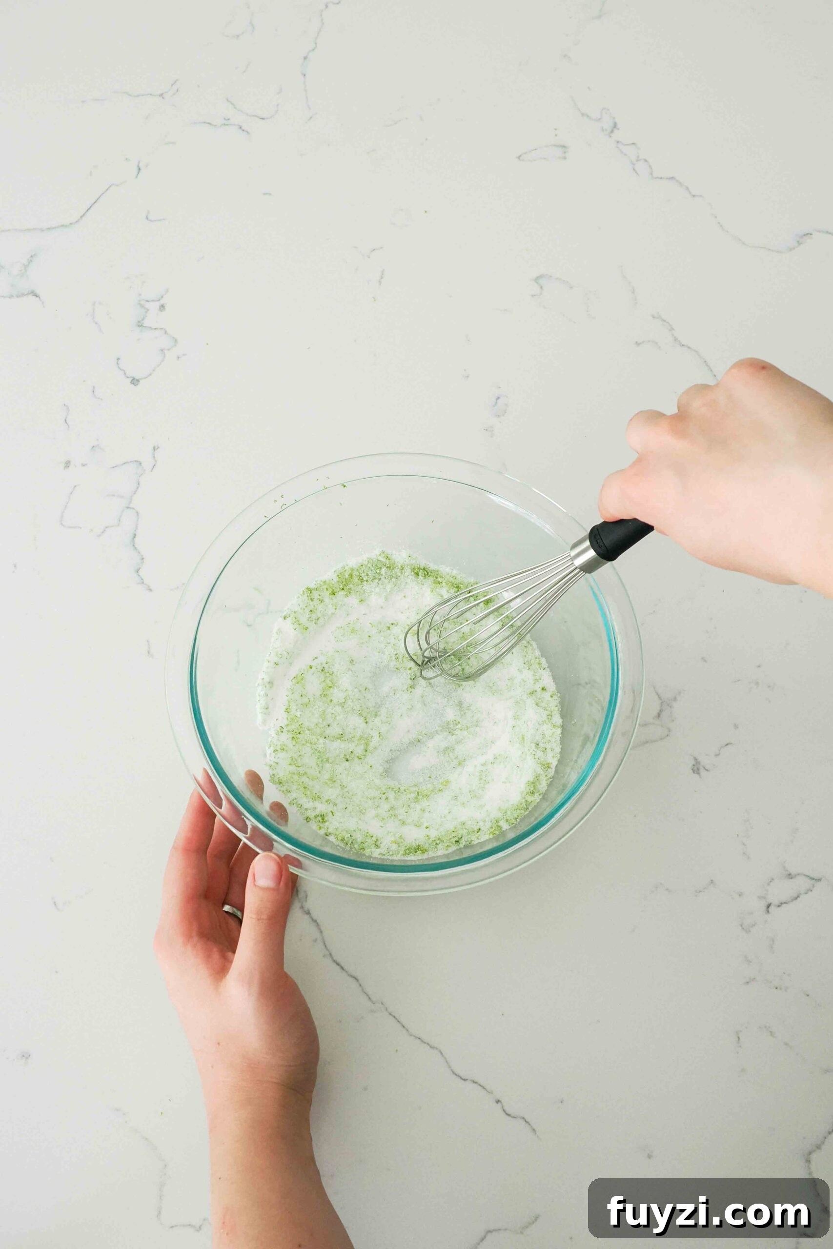 Lime zest is whisked into sugar in a glass bowl.