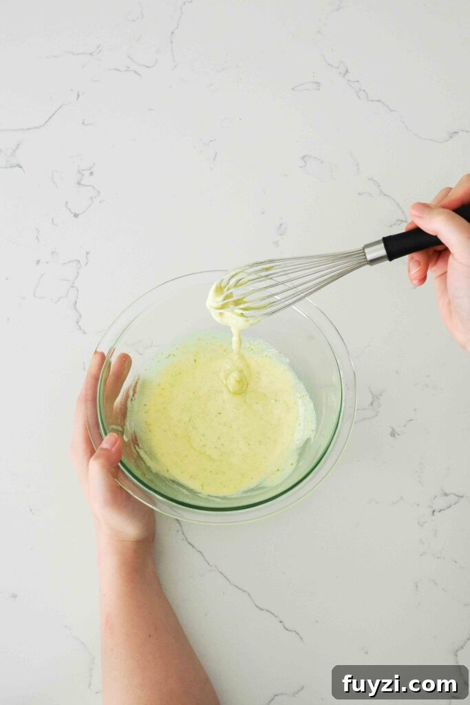 A whisk holds up lime custard whisked to the ribbon stage.