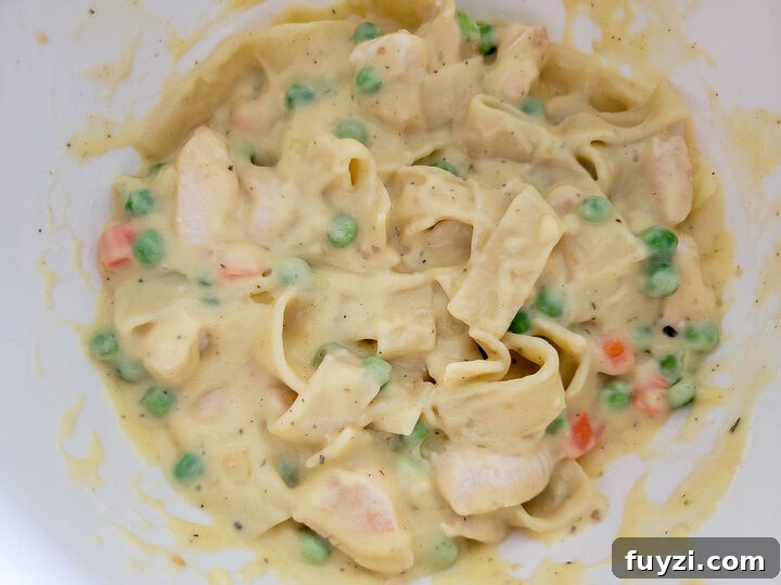 Creamy Chicken Noodle Casserole with Golden Crust 5 chicken, peas, carrots, thick egg noodles, and creamy sauce in a bowl.