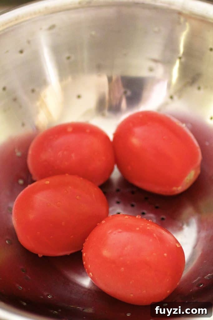 Photo of four tomatoes in stainless steel colander.